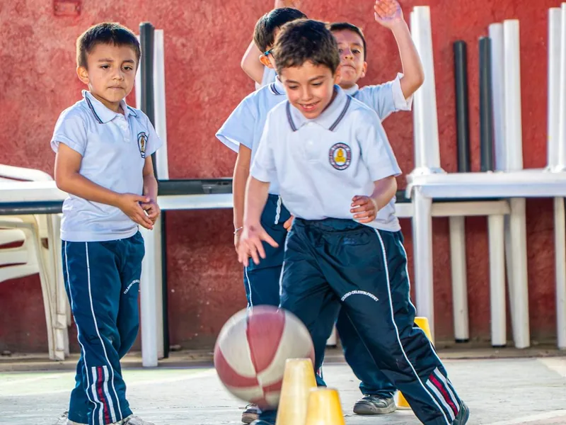 Niños con uniforme deportivo juegan con un balón de baloncesto en una zona cubierta.